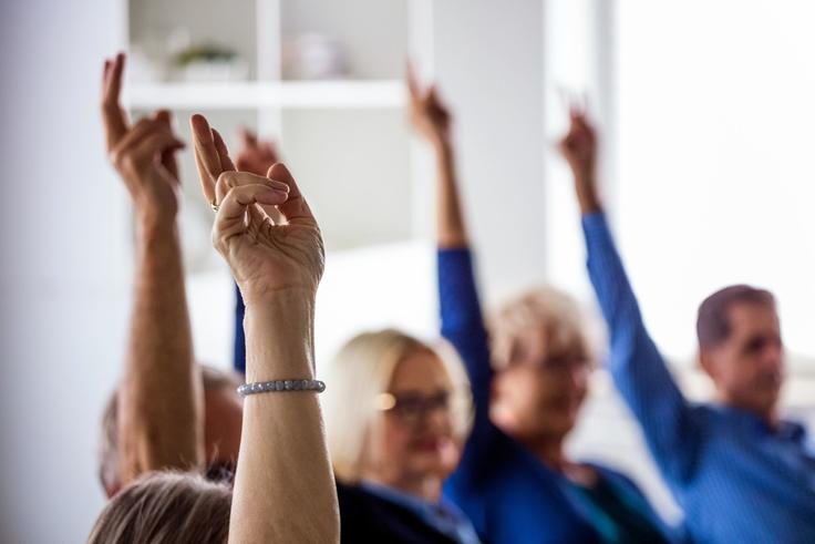 People seated in a room, raising their hands, focused on participation.