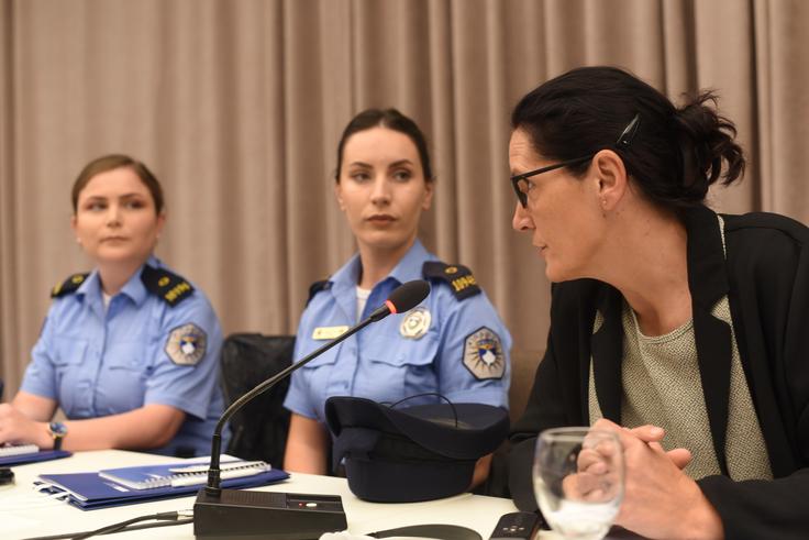 Three women in a panel discussion, two in police uniforms and one in civilian attire, with microphones and papers on the table.